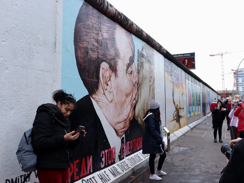 The East Side Gallery in Berlin. The painting show is "My God, Help Me To Survive This Deadly Love" by Dmitri Vrubel, which shows a kiss between Erich Honecker and Leonid Brezhnev. Large crowds swarm around it to try and take a photo.