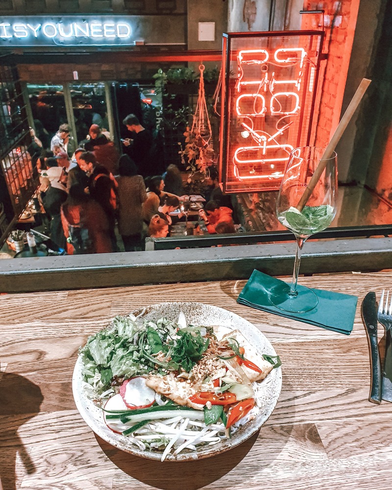 On the table is a bowl of delicious noodles with tofu and vegetables. Pho restaurant in Berlin is visible in the background