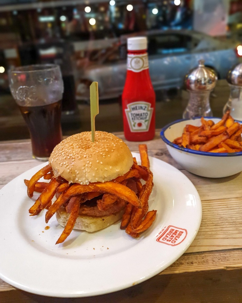 Vegan burger at Bread Meats Bread Edinburgh. Inside the seed-topped bun is a vegan patty with fake bacon. It's also overflowing with sweet potato fries!